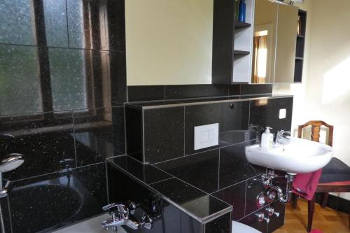 Baño de azulejos negros con lavabo y espejo en Ferienwohnung Villa Haniel Edmund, en Dresden
