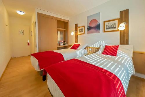 two beds in a hotel room with red and white sheets at Hotel des Alpes Bulle center in Bulle