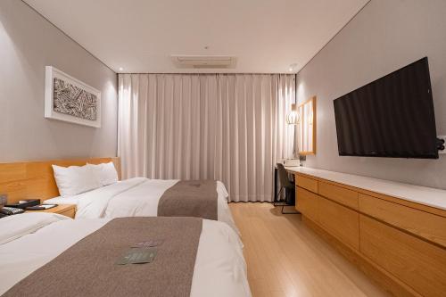 a hotel room with two beds and a flat screen tv at Gloucester Hotel Cheongju in Cheongju