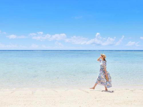 Una mujer caminando por la playa cerca del agua en Hotel Nikko Alivila, en Yomitan