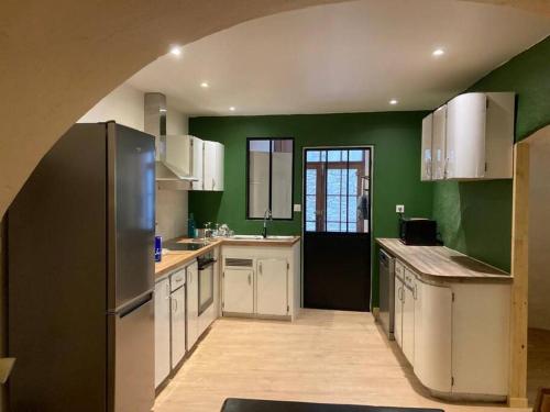 - une cuisine avec des murs verts, des armoires blanches et un réfrigérateur dans l'établissement Appartement Rez-de-chaussée, à Largentière
