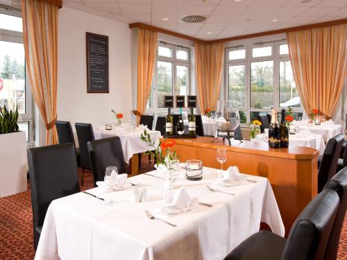 a restaurant with white tables and chairs and windows at ACHAT Hotel Schwarzheide Lausitz in Schwarzheide
