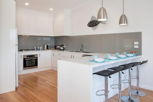 a kitchen with white cabinets and a counter with stools at Minnamurra Beach Bliss Minnamurra in Minnamurra