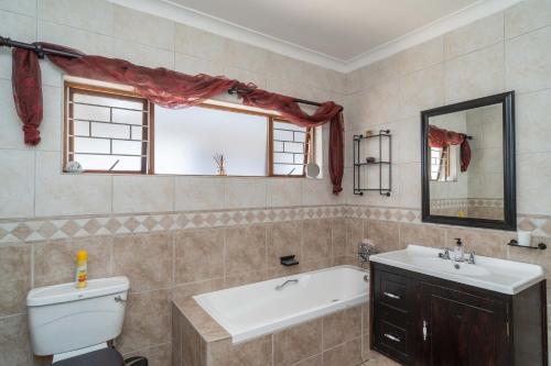 een badkamer met een bad, een wastafel en een toilet bij Spacious retreat with large pool and lush garden in Pinetown