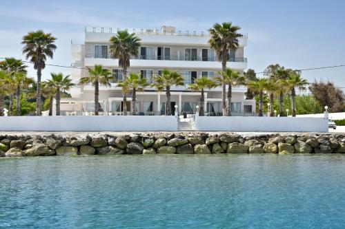 a white building with palm trees in front of the water at Sidari Beach Hotel in Sidari