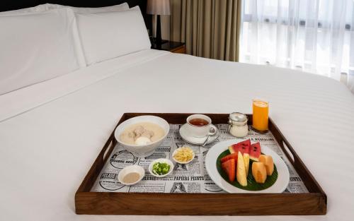a tray of food on a bed with a plate of fruit at Chatrium Sathon Bangkok in Bangkok