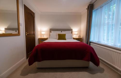 a bedroom with a bed with a red blanket and a window at Charnwood Guest House in Bracknell