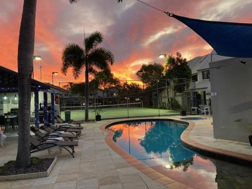 a swimming pool with chairs and a sunset in the background at Nautilus Noosa Resort in Noosaville