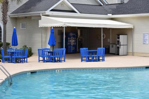 a pool with blue chairs and umbrellas next to a house at Close to Beach Brunswick Plantation Condo 2302M with 27 Hole Golf Course Onsite condo in Calabash