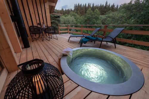 a hot tub on a deck with chairs and tables at Forstgut - Premium Waldchalets und Lodge Suiten in Regen