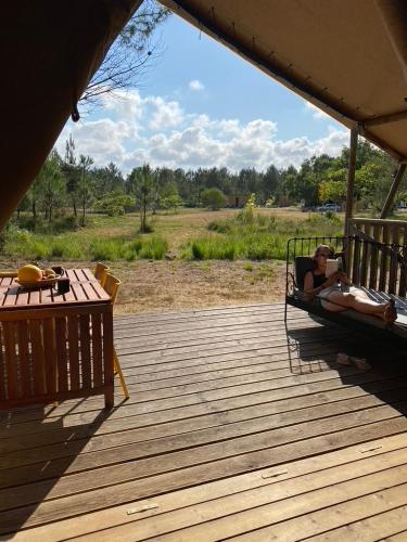 a woman laying in bed on a wooden deck at Camping la Kahute - Tente lodge au coeur de la forêt in Carcans