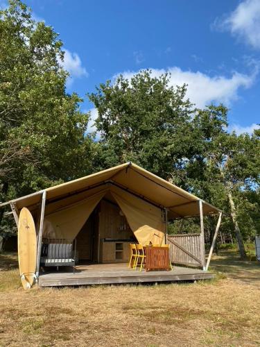 a tent with a table and chairs in a field at Camping la Kahute - Tente lodge au coeur de la forêt in Carcans