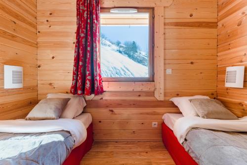 two beds in a log cabin with a window at travelski home select - Chalets Le Grand Panorama II 3 stars in Valmeinier