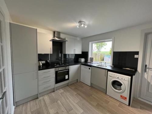 a kitchen with white cabinets and a washing machine at Walk to Everything in Crail - Land Sea Cottage in Crail
