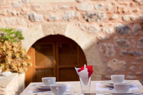 a table with plates and cups and a vase with a red flower at Theophano Art Hotel in Monemvasia