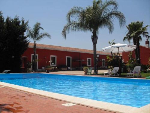 una piscina frente a un edificio rojo con palmeras en Mediresidence Maeggio, en Contrada Maeggio