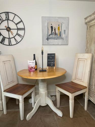 a table with two chairs and a clock on the wall at Hollies Cottage in Keighley