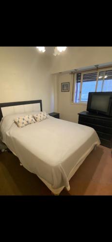 1 dormitorio con 1 cama blanca grande y TV en 3 ambientes barrio norte en Buenos Aires