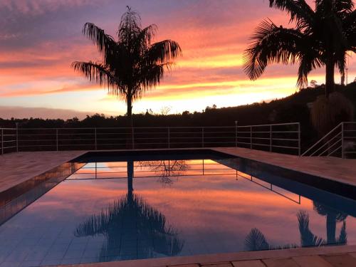 einen Pool mit einer Palme vor einem Sonnenuntergang in der Unterkunft Chácara em Mairinque - Porta do Sol com seg 24 hs in Mairinque