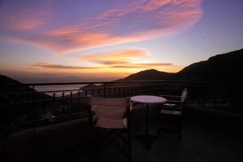 a table and chairs on a balcony with a sunset at Stone house with panoramic view in Tiros