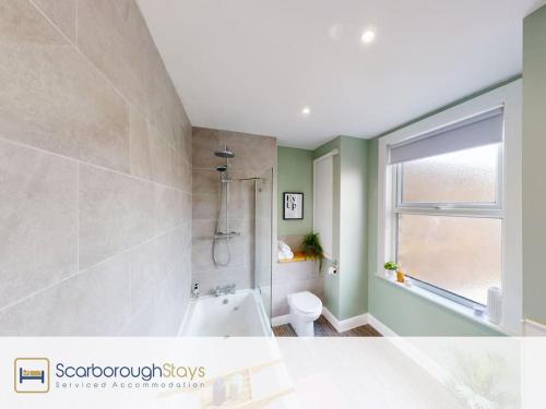a bathroom with a tub and a toilet and a window at Scarborough Stays - Norwood House in Scarborough