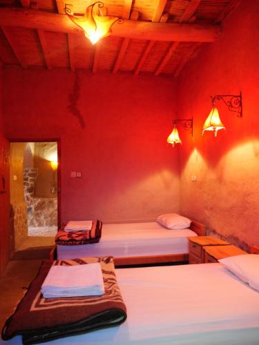 two beds in a room with red walls and lights at Chambres dans casbah - Gite D'étape Gorges De Ziz in Er Rachidia