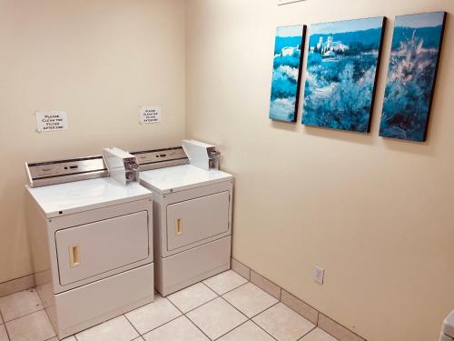 two washing machines in a laundry room with two paintings at Aurora Park Inn & Suites in Dawson Creek