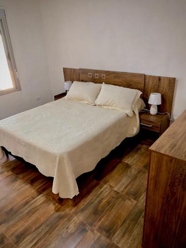 um quarto com uma cama com lençóis brancos e pisos em madeira em Casa pet friendly, se reserva con seña em Piriápolis