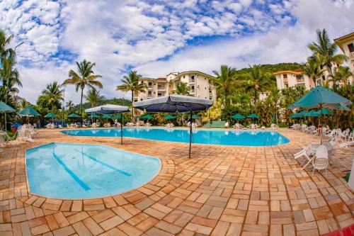 a pool at a resort with palm trees and umbrellas at Apartamento Wembley Tenis - Ubatuba 33 in Ubatuba