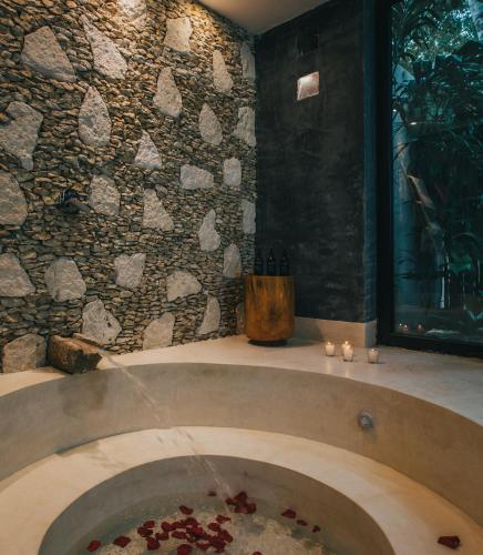 a bathroom with a tub with a stone wall at Yum Kaax Boutique Villa in Tulum