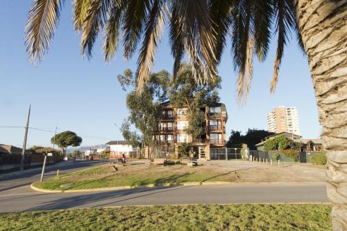 an apartment building on a street with a palm tree at Linda Vista Apart Hotel in Concón