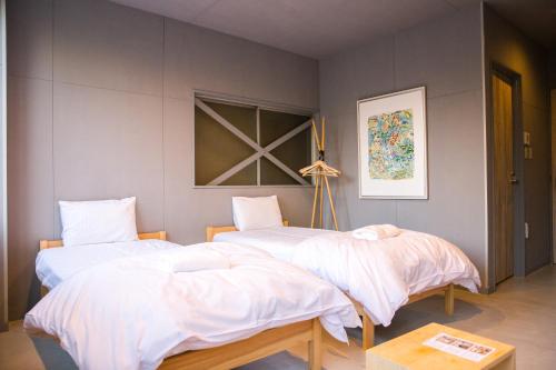 2 Betten mit weißer Bettwäsche in einem Zimmer in der Unterkunft Hostel STAND BY ME in Fukuoka