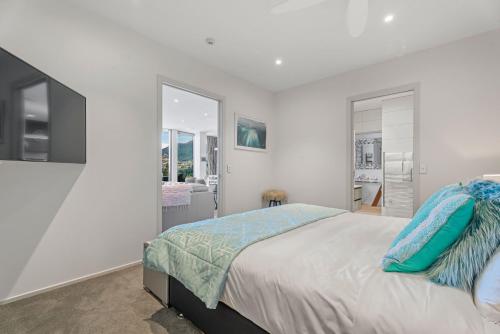 a white bedroom with a large bed with blue pillows at Chic Central Penthouse & Spa by Staysouth in Queenstown