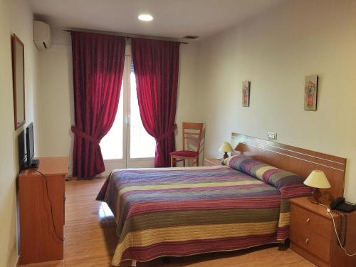 1 dormitorio con 1 cama y una ventana con cortinas rojas en Hotel Godofredo, en Toledo