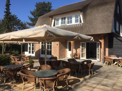 a patio with tables and chairs and an umbrella at Herberg het Landhuis in Schoorl