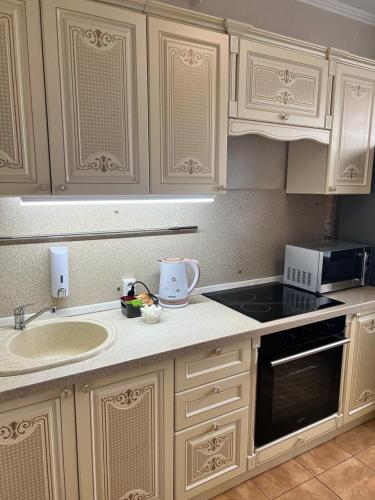 een keuken met witte kasten, een wastafel en een fornuis bij Квартира бизнес класса in Semey