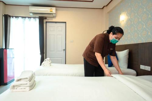 a woman making a bed in a hotel room at Blue Sky Residence Airport in Ban Bang Phli Yai