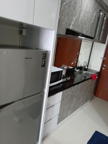 a small kitchen with a refrigerator and a sink at Palam Mansion at Meisterstadt Pollux Habibie Apartment in Batam Center