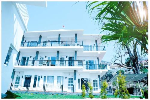 a white building with a balcony and a palm tree at The Periwinkle Homestay Bhimtal in Bhīm Tāl