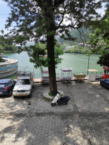 a motorcycle parked next to a tree next to a lake at The Periwinkle Homestay Bhimtal in Bhīm Tāl