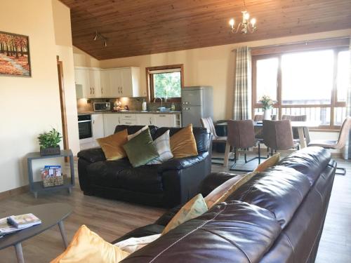 a living room with a leather couch and a kitchen at Silver Birch Lodge with Hot Tub in Cupar