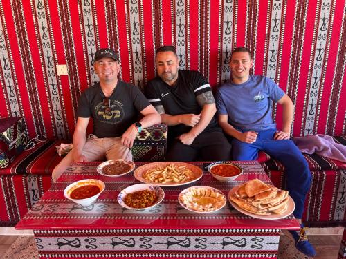 a group of three men sitting around a table with food at Wadi Rum Mars Camp in Wadi Rum