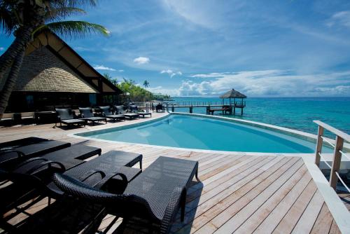 a swimming pool with chairs and the ocean in the background at Maitai Rangiroa in Avatoru