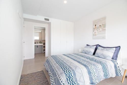 a white bedroom with a bed with blue and white sheets at Global Properties, Apartamento con terraza y vistas a la piscina en Gran Canet in Canet de Berenguer