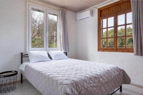 a bedroom with a bed with white sheets and two windows at Salty Pebble House in Fiskardho