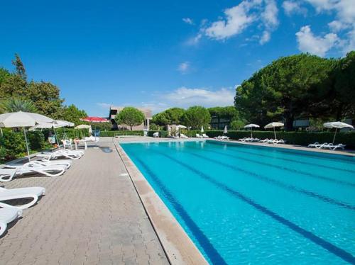 a large swimming pool with white chairs and umbrellas at Premium Apartment Bilo H2 in Marina di Bibbona