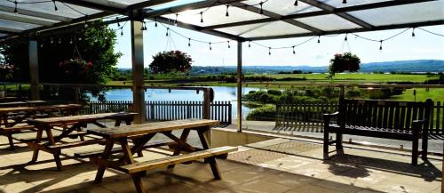 un patio con tavoli, panche e vista sul lago di Gateway Glamping Pods a Llanelli