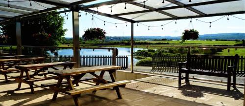 a patio with tables and benches and a view of a lake at Gateway Glamping Pods in Llanelli