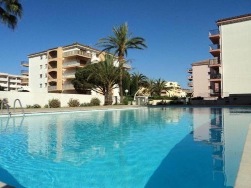 une grande piscine avec des palmiers et des bâtiments dans l'établissement Sainte-Maxime, Apt 2 pièces avec piscine, terrasse, parking privé, proche plage et commerces - FR-1-226-487, à Sainte-Maxime