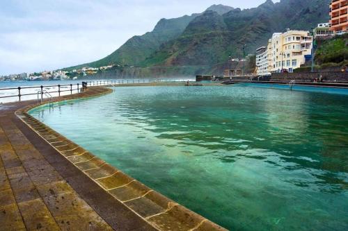 a pool of green water with mountains in the background at Osa Mayor Apartment Bajamar in Bajamar